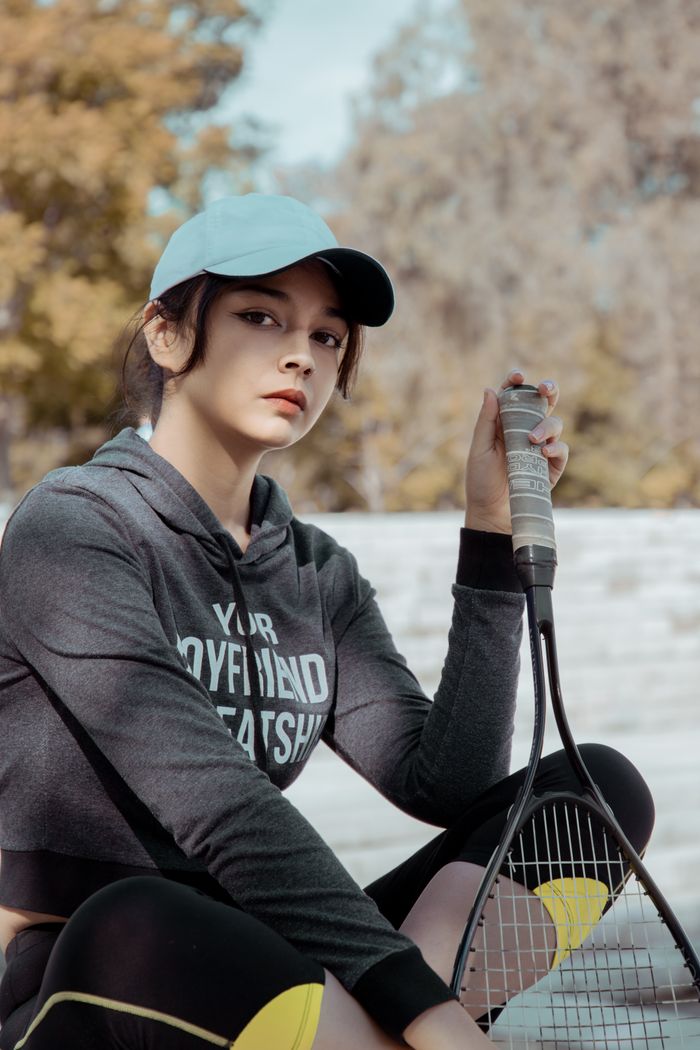 Confident young woman holding a tennis racket outdoors in casual sportswear and cap.