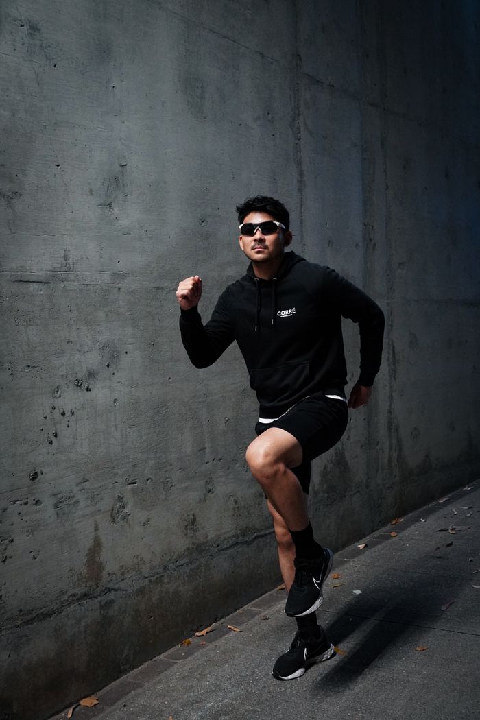 Young man in motion, wearing trendy streetwear running against a gritty urban backdrop.