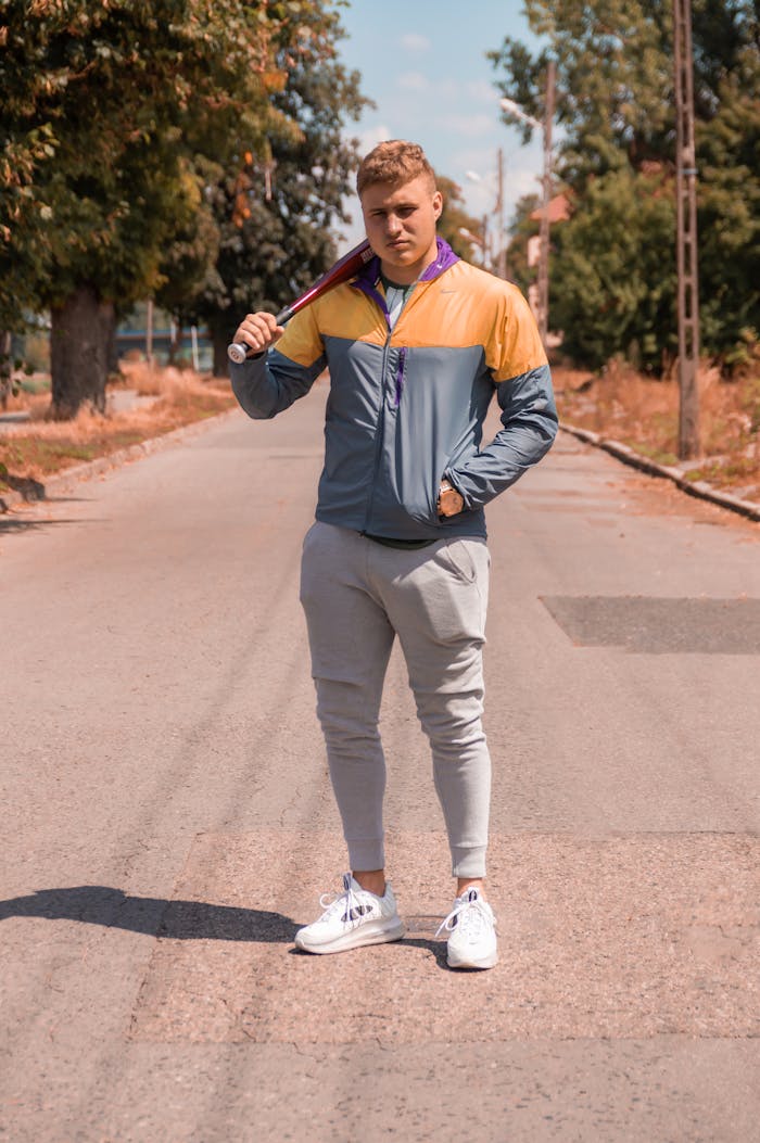 Full body sportive man holding bat and looking at camera standing on roadway while looking at camera
