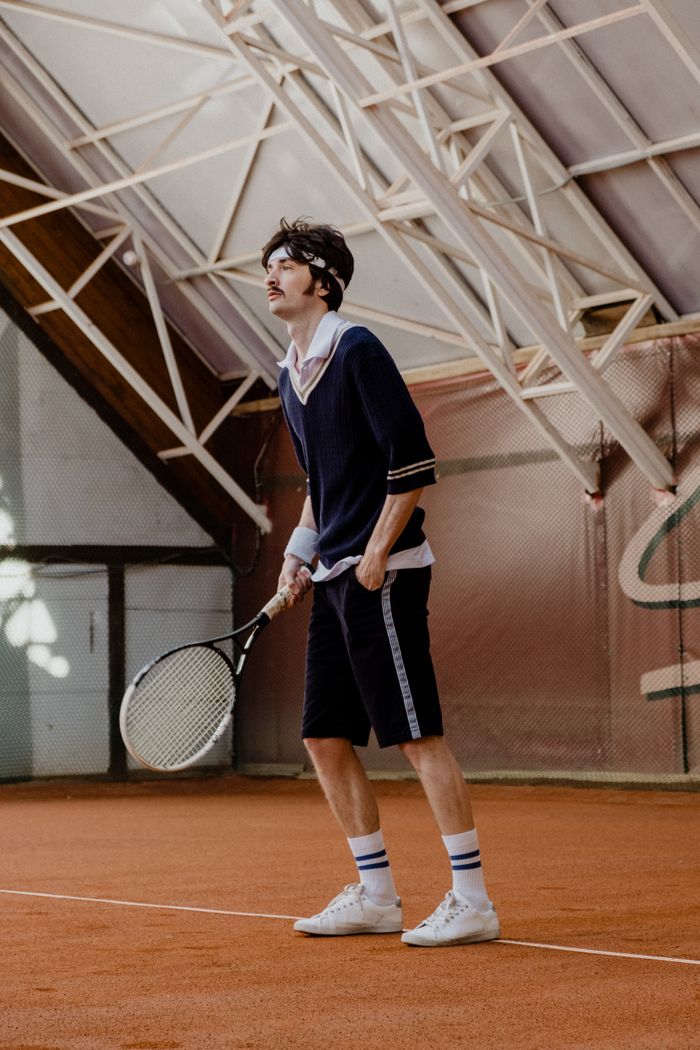 Young man holding a tennis racket on an indoor clay court, preparing to play a match.